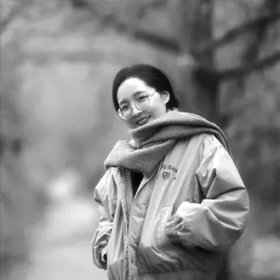Young woman wearing winter parka and scarf smiles at camera while standing outdoors.